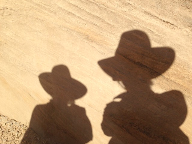 Shadows of "Indiana Jones" style hats in the sand.