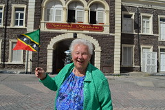 Theresa Irene Wolowski waving The flag of Saint Kitts and Nevis at the National Museum Gateway to Historic Basseterre, on the island of Saint Kitts