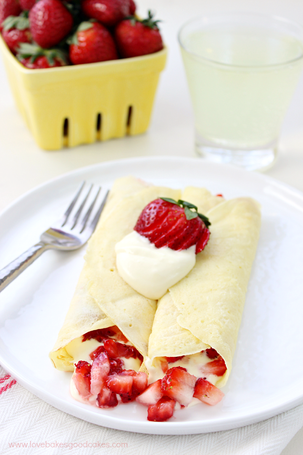 Strawberry & Lemon Cream Crepes on a white plate with a fork and fresh strawberries.