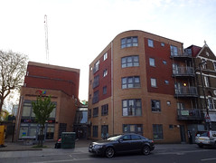 A modern-looking building with a curved corner towards the front, in dark red and sandy-coloured bricks, with lots of windows.  Another building in the same colours but with fewer windows and the name “Croydon Voluntary Action” on the front is to its left.