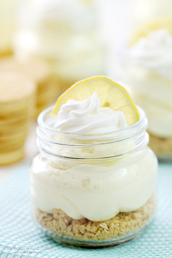 No-Bake Lemon Cheesecake in glass jars with a slice of lemon close up.