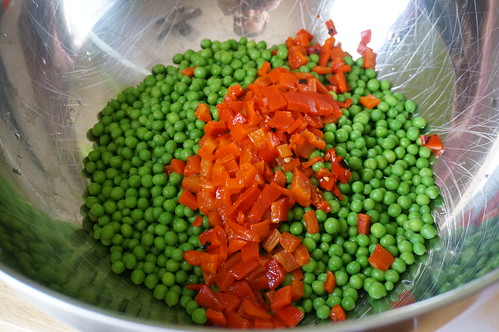A line of diced red pepper sits on top of a bed of peas in a large metal bowl