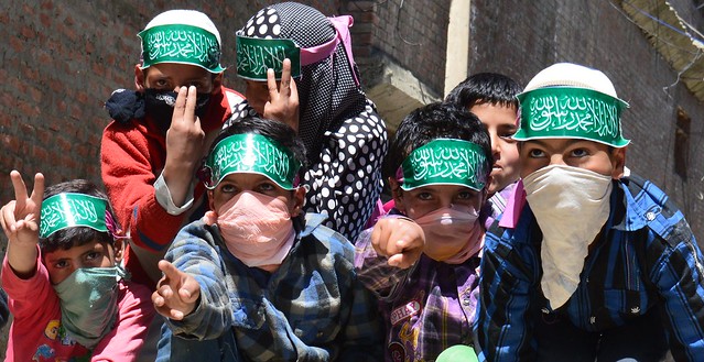 A group of kids wearing piece of painted green paper inscribed with Quranic verses and showing victory story sign in Narbal Town of Central Kashmir Budgam District
