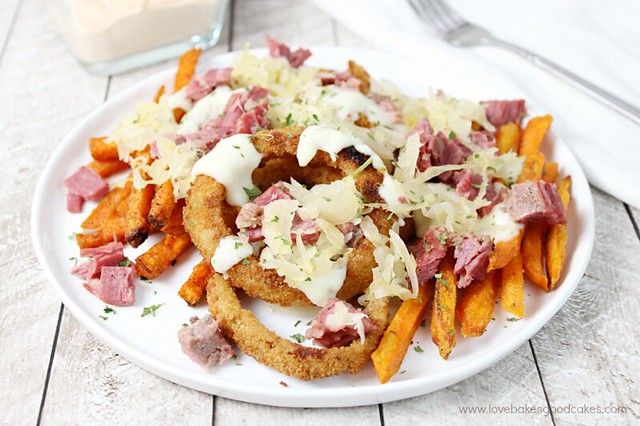 Reuben Fry Basket with onion rings and sweet potato fries on a white plate with a fork.