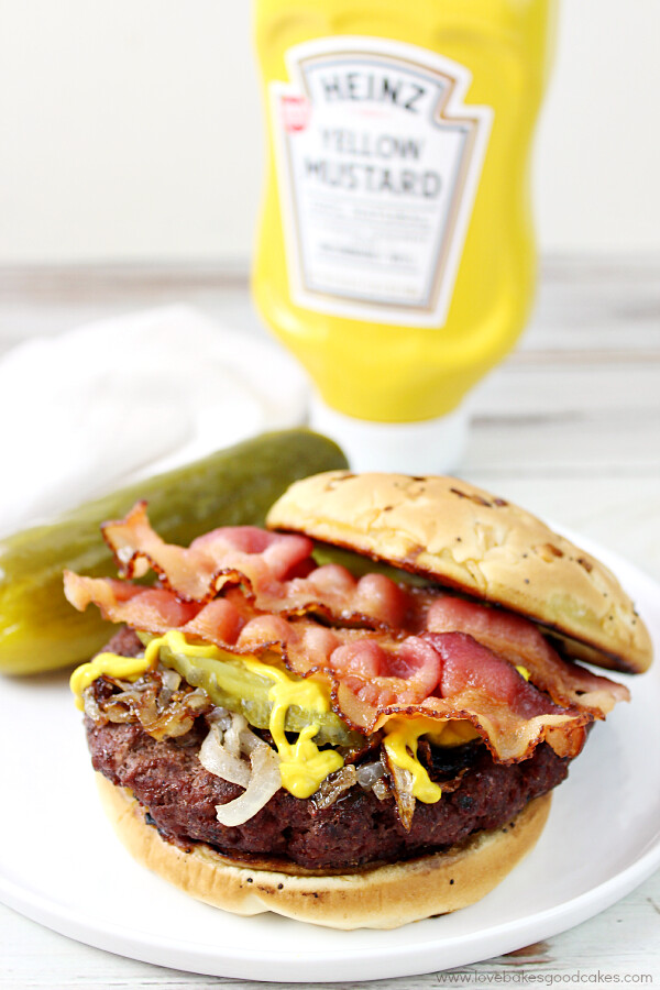 Rouladen Burger on a plate with a pickle and a bottle of yellow mustard. 