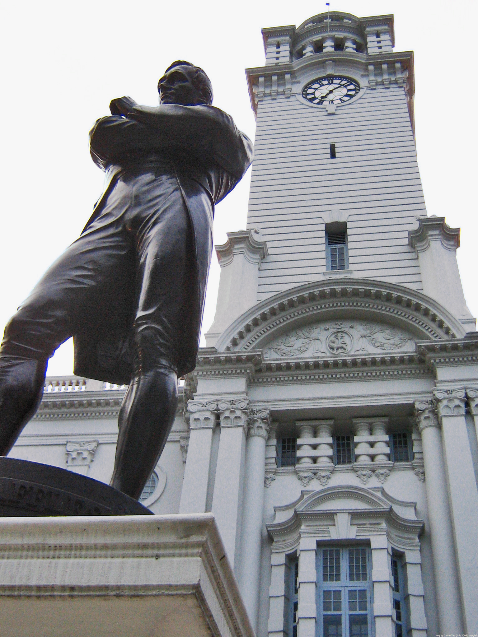 Statue of Stamford Raffles by Thomas Woolner in front of the clock tower of the Victoria Theatre and Concert Hall in Singapore (originally called Victoria Memorial Hall). On February 6, 1919, during celebrations of the centenary of Singapore's founding,this statue was moved from the Padang to the front of the Memorial Hall. The statue was complemented with a new semicircular colonnade and a pool. Photo taken by Calvin Teo on July 6, 2006. 