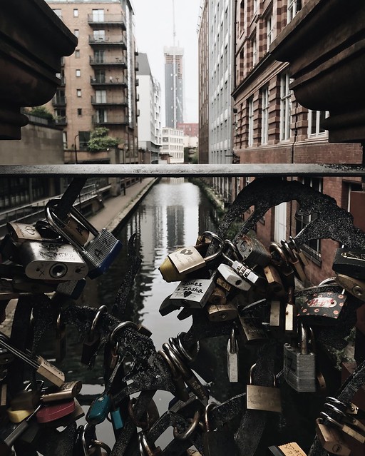 A close up of dozens of locks on a metal bridge over a canal cutting through tall buildings. 