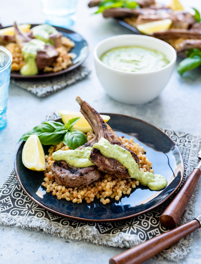grilled lamb chops on blue plates with green herbed tahini sauce fresh basil lemon wedges
