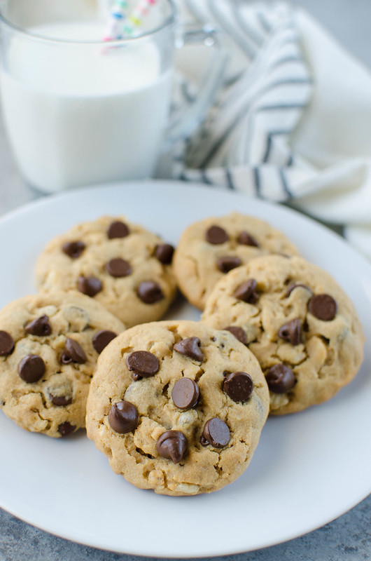 5 peanut butter chocolate chip cookies on a white plate with a glass of milk in the background