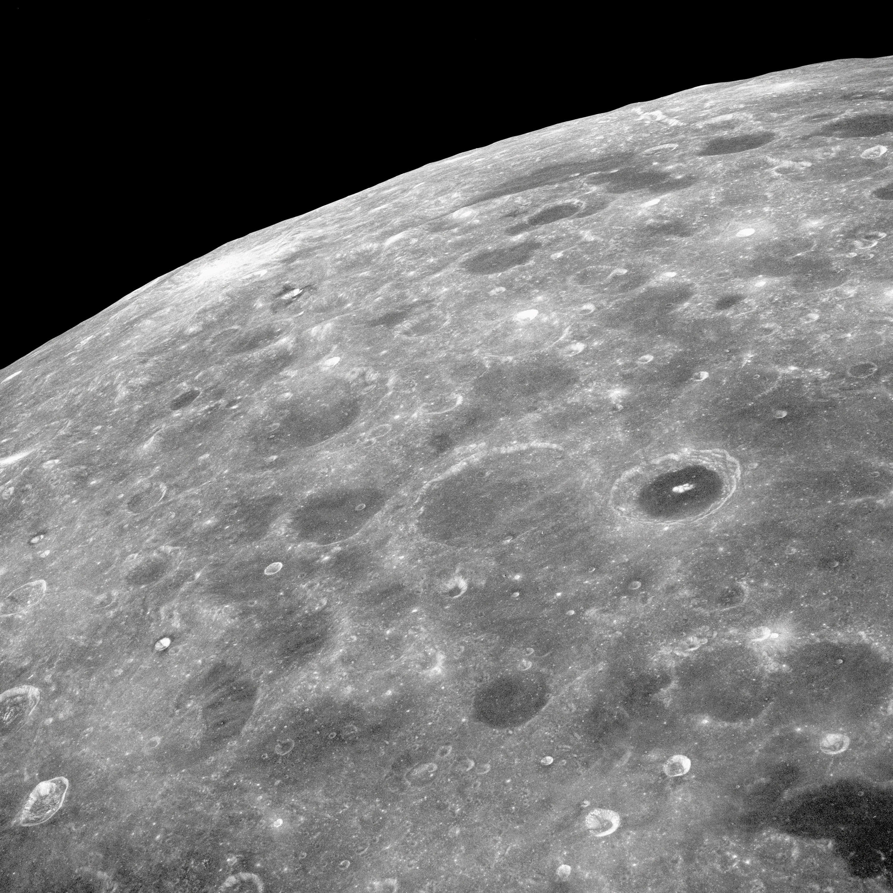 View of the lunar surface taken from the Apollo 8 spacecraft looking southward from high altitude across the Southern Sea. The bright-rayed crater near the horizon is located near 130 degrees east longitude and 70 degrees south latitude. The dark floored crater near the middle of the right side of the photograph is about 70 kilometers (45 statute miles) in diameter. Both features are beyond the eastern limb of the Moon as viewed from earth; neither has a name.