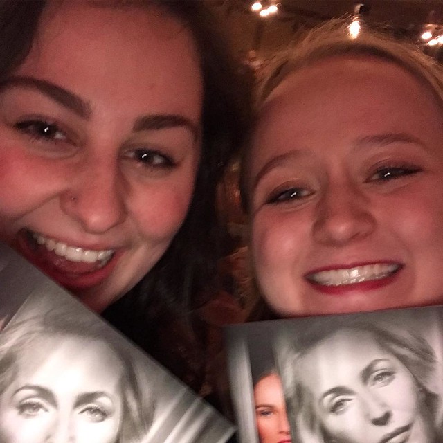 Two girls holding up playbills of with a woman's face on them. 