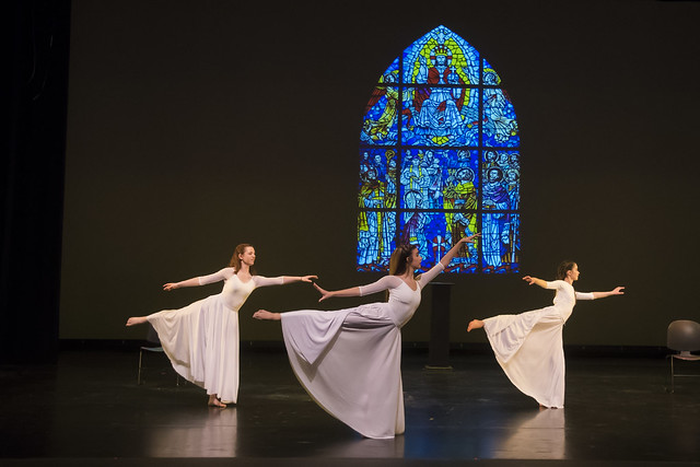 Three dancers perform on stage in front of a stained glass window during a production of Dancing Community.