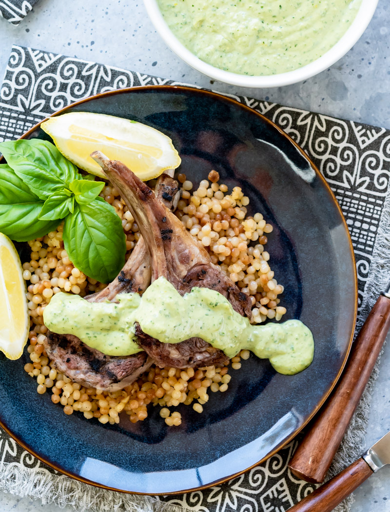 grilled lamb chops on blue plates with green herbed tahini sauce fresh basil lemon wedges