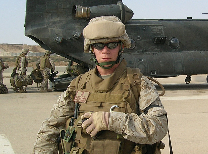A Marine in uniform stands in front of a military helicopter.
